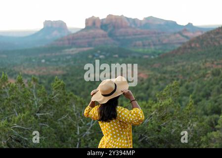 Frau in einem gelben Pünktchen-Kleid, mit Hut und Blick auf rote Felsen. Stockfoto