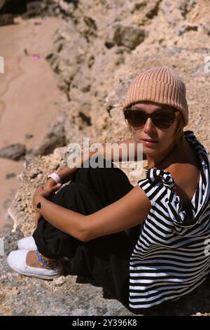 Frau, die auf einer felsigen Klippe in Sagres, Algarve, Portugal sitzt. Stockfoto