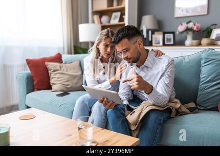 Eine junge Geschäftsfrau tröstet ihren Mann zu Hause, während er negative Statistiken über den Handel seines Unternehmens auf einem digitalen Tablet liest. Zusammengehörigkeit Stockfoto