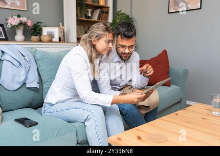 Eine junge Geschäftsfrau tröstet ihren Mann zu Hause, während er negative Statistiken über den Handel seines Unternehmens auf einem digitalen Tablet liest. Zusammengehörigkeit Stockfoto