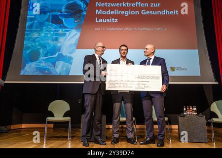 13. September 2024, Brandenburg, Cottbus: Dietmar Woidke (SPD, l-r), Ministerpräsident Brandenburgs, Ulrich Scheppan, Vorsitzender des Vorstands der Brandenburgischen Investitionsbank und Eckhard Nagel, Vorsitzender des Vorstands und Direktor des Gesundheitswesens der Medizinischen Universität Lausitzer - Carl Thiem, stehen bei der symbolischen Übergabe von Strukturstärkungsfonds in Höhe von 85 Millionen Euro auf der länderübergreifenden Netzversammlung der Modellregion Lausitzer Lausitzer Healthcare Seite an der Bühne. Auf dieser gemeinsamen Konferenz mit Interessenvertretern aus dem Gesundheitswesen, Universitäten, Verbänden und pu Stockfoto