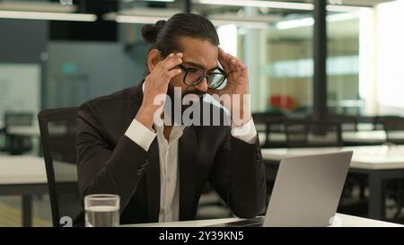 Gestresster kranker indischer männlicher Arbeitgeber Unternehmen arabischer Unternehmer Boss CEO Geschäftsmann muslimischer Geschäftsmann im Büro mit Laptop arbeitet Stockfoto