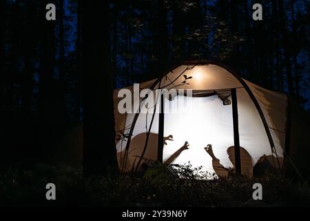 Silhouetten von Kindern, die nachts im Campingzelt spielen und während der Sommerferien Schattenpuppen mit Taschenlampe machen Stockfoto