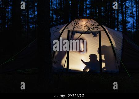 Silhouetten von Kindern, die nachts im Campingzelt spielen und während der Sommerferien Schattenpuppen mit Taschenlampe machen Stockfoto