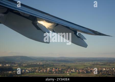 Die untergehende Sonne scheint auf die Mechanismen unter einem Linienflugzeugflügel, während er von Zürich aus startet Stockfoto