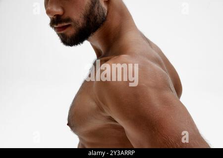 Zugeschnittenes Foto von Brust und Schultern des Mannes, das Licht wirft weiche Schatten, die seinen muskulösen Aufbau vor weißem Hintergrund definieren. Stockfoto