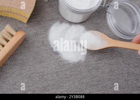 Die Hand einer Frau verwendet natürliche Zutaten Backpulver, um Tintenflecken auf grauen texturierten Polstern eines Sofas oder Teppichs zu entfernen. Draufsicht Stockfoto