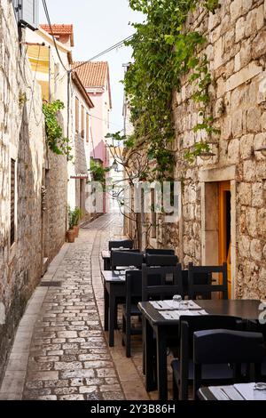 Leere Restauranttische im Freien säumen eine schmale Kopfsteinpflastergasse in Stari Grad Stockfoto