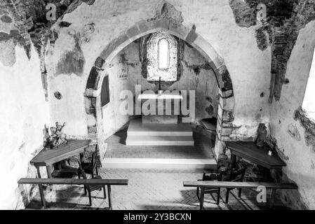 Ein ruhiger Blick auf die mittelalterliche Kapelle im Schloss Aggstein mit Blick auf den Altar, das Bogenfenster und rustikale Holzbänke unter weichem Tageslicht. Wachau, Österreich. Schwarzweißfoto Stockfoto