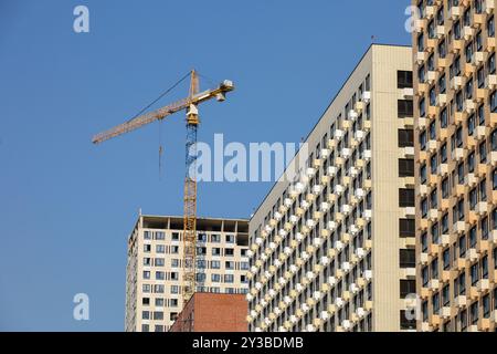 Turmkran und unfertige Gebäude auf blauem Himmel. Wohnungsbau, Wohnblöcke in der Stadt Stockfoto