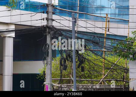 Elektromasten mit unordentlichen Drähten, unordentlich verwickelten Strom- und Telekommunikationskabeln an den Masten an der Seite einer Stadtstraße Stockfoto