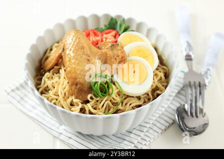 Indomie Rebus oder Instant Boiled Nudeln mit Soto-Geschmack, indonesische Instant Nudeln mit geschnittenem gekochtem Ei, Tomaten und Hühnerflügel Stockfoto