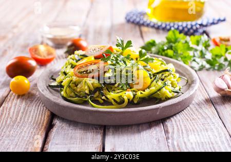 Zucchini Nudeln mit Pesto, Avocado und Tomaten auf einem grauen Teller. Rohes veganes Food-Konzept. Stockfoto