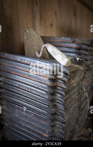 Viele Dachziegel in einer Scheune gestapelt, oben ein alter Spatel, Spinnweben, Hintergrund Holzwand, Wallonien, Belgien, Europa Stockfoto