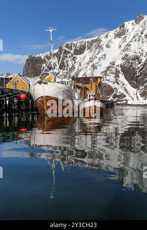 Fischerboote, Fischerdorf mit gelben Häusern vor verschneiten Bergen, Nusfjord, Flakstadoya oder Flakstadoy, Insel Vestvagoya, Lofoten, Noch Nicht Stockfoto