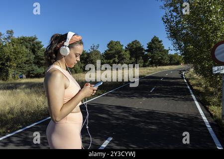 Junge Frau, die Musik auf einer Asphaltstraße an einem sonnigen Tag hört, Runner Woman, die Musik mit Kopfhörern auf einer Asphaltstraße hört. Konzept von ru Stockfoto