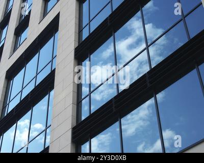 Schräger Blick auf ein modernes Geschäftsgebäude mit großen Spiegelfenstern, die blauen Himmel und weiße Wolken reflektieren Stockfoto