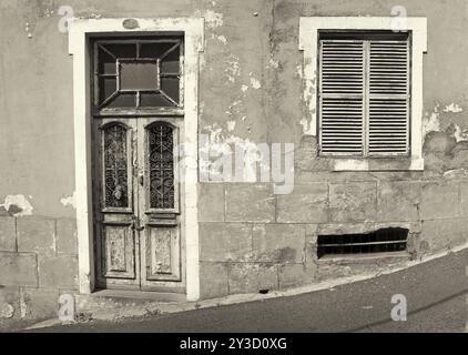 Die Vorderseite eines alten verlassenen Hauses mit verschlossenen Fenstern und verschlossener Holztür mit abblätternder Farbe auf einem schrägen, monochromen Straßenbild Stockfoto