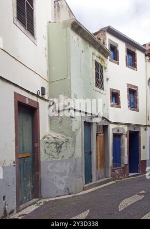 Eine typische ruhige, leere Straße in funchal madeira mit alten, traditionellen Häusern, die mit verblasster Pastellfarbe bemalt sind, und einer Kopfsteinpflasterstraße Stockfoto