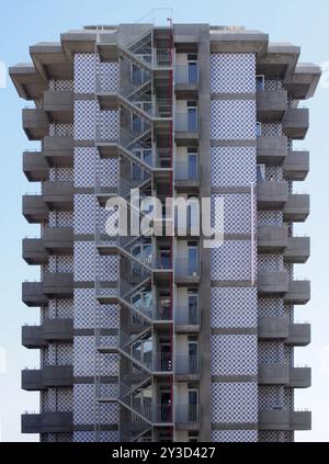 Ein alter hoher Betonwohnungsblock mit sich wiederholenden Betonbalkonen und einer Außentreppe mit Metallgeländern gegen einen blauen Himmel Stockfoto