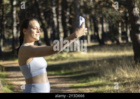 Lächelnde junge Sportlerin, die ein Selfie mit ihrem Handy macht, während sie in der Wildnis trainiert Stockfoto
