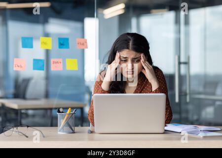 Verärgerte und müde Frau, die im Büro am Arbeitsplatz sitzt, Geschäftsfrau, die sich auf die Arme stützt und elektronische Berichte liest, Mitarbeiter des Unternehmens, die mit dem Ergebnis der Teamarbeit nicht zufrieden sind. Stockfoto