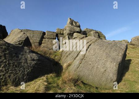 Große, zerklüftete Gritsteinausläufer an den Bridestonen einer großen Felsformation in West yorkshire in der Nähe von todmordendem blauem Himmel und umliegender Landschaft Stockfoto