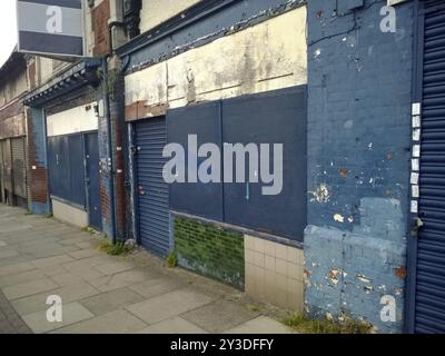 Eine Reihe verlassener Geschäfte mit verschlossenen Ladenfronten mit zerbröckelnden Fassaden und abblätternder blauer Farbe in einer städtischen Straße Stockfoto