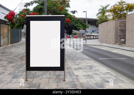 Leere Plakate in einer Bushaltestelle auf der Straße mit farbenfrohen roten Blumenbäumen im Hintergrund Stockfoto