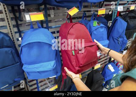 Eine Frau hält einen roten Rucksack in einem Laden. Es gibt viele Rucksäcke, darunter blaue und grüne. Back-to-School-Konzept Stockfoto