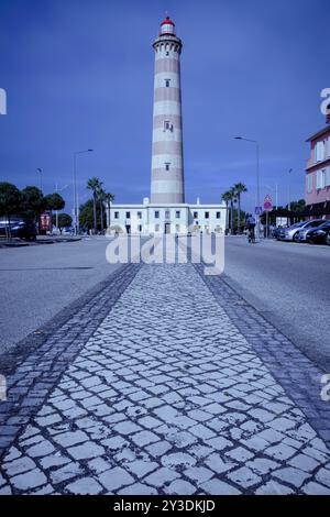 Majestätischer Leuchtturm in Praia da Barra, Aveiro - Nautical Beacon gegen Kopfsteinpflasterpfad und Blue Sky Stockfoto