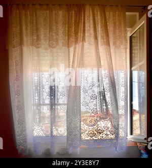 Heiße Nachmittagssonne durch halb geschlossene Jalousien draußen offene doppelt verglaste Fenster mit Netzvorhängen in einem Dorf in Spanien Stockfoto