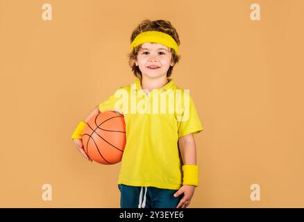 Lächelndes Kind in Sportbekleidung mit Basketballball. Sportausrüstung. Kleiner Basketballspieler mit Ball. Fitness, Training und aktiver Lebensstil für Kinder. Korb Stockfoto