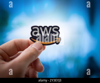 LOS ANGELES, KALIFORNIEN - 1. Juni 2024: Menschliche Hand hält Amazon Web Services AWS-Logo-Aufkleber vor einem leuchtenden, verschwommenen Computerbildschirm. Closeu Stockfoto