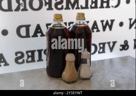 Essig-, Salz- und Pfefferflaschen auf einem Tisch vor einem Café-Fenster mit umgekehrter Schrift. Stockfoto
