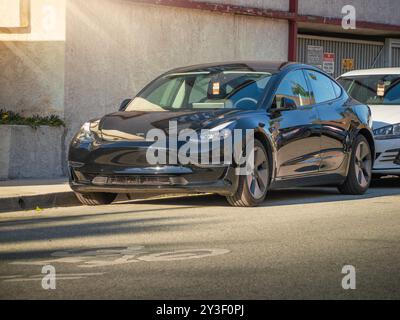LOS ANGELES – 17. Juli 2024: Tesla Model 3 parkt bei Sonnenuntergang auf der City Street in West Hollywood, Kalifornien. Stockfoto