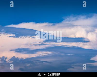 Blauer Himmel mit weißen, stürmischen Cumulus-Wolken, die durch niederlagige Regenwolken gesehen werden. Stockfoto