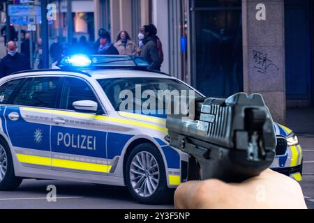 Bayern, Deutschland - 13. September 2024: Person zeigt Waffe auf deutsches Polizeifahrzeug oder Polizeipatrouillenwagen. Konzeptverbrechen und Straftaten mit dem Einsatz einer Schusswaffe oder Waffe. PHOTOMONTAGE *** Person richtet Waffe auf deutsches Polizeifahrzeug, bzw. Einsatzwagen der Polizei. Konzept Verbrechen und Straftaten mit dem Einsatz einer Schusswaffe, bzw. Waffe. FOTOMONTAGE Stockfoto