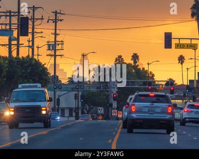 Autos säumen im abendlichen Verkehr auf einer Stadtstraße in der Abenddämmerung mit Palmensilhouetten und entfernten Gebäuden der Skyline VON Downtown LA, die sich gegen DRAM erheben Stockfoto