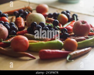 Horizontale Nahaufnahme von blauen Trauben, Tomaten, Äpfeln und bunten Chili Paprika auf Holztisch Stockfoto