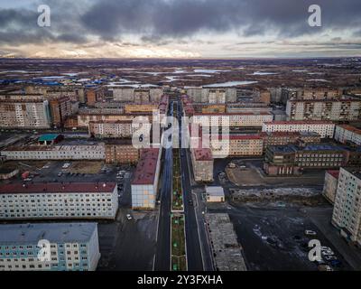 Das Panorama der Stadt Norilsk im Norden der russischen Arktis (Region Krasnojarsk) mit den dunklen sowjetischen Gebäuden, dem Tundrafeld, dem bewölkten Himmel und der Stadtstraße. Stockfoto