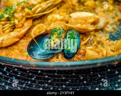 Das traditionelle spanische Meeresfrüchte-Gericht Paella in einer schwarzen Pfanne mit Muscheln und Garnelen auf einem Reisblock Stockfoto