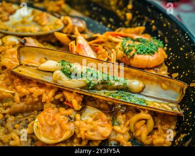 Das traditionelle spanische Meeresfrüchte-Gericht Paella in einer schwarzen Pfanne mit Muscheln und Garnelen auf einem Reisblock Stockfoto