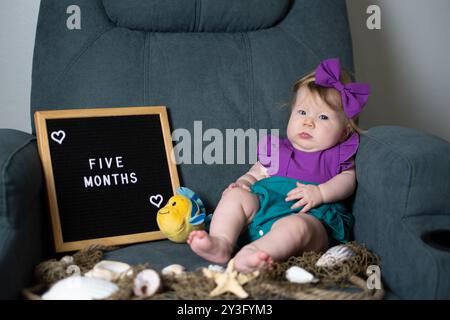 Süßes weißes Mädchen in einem Meerjungfrauenkostüm. 5 Monate altes Baby mit Filzbrieftafel zum Mini-Geburtstag. Monatliche Fotoshooting-ide für Babybilder Stockfoto