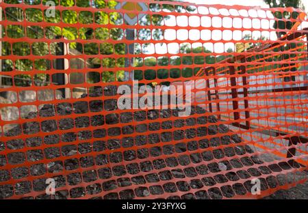 Eine Baustelle mit orangefarbenem Sicherheitsnetz, in dem die Barrieren und die Arbeiten an der städtischen Infrastruktur hervorgehoben werden. Stockfoto