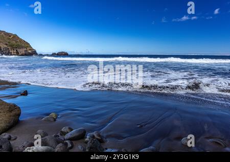 Strand mit schwarzem vulkanischem Sand, grüne Palmen am Hang, gefährliche Wellen, Atlantik, Castro Beach Playa Castro Teneriffe Spanien Stockfoto