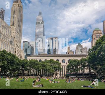 Blick auf die Menschen, die sich im Bryant Park in New York City an einem schönen Sommertag entspannen; Wolkenkratzer und Himmel im Hintergrund Stockfoto