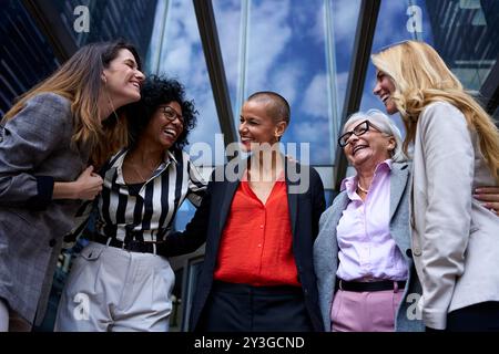 Kleiner Winkel von Team aus verschiedenen Geschäftsfrauen, die glücklich zusammen lachen beim Eingang von Modern Stockfoto