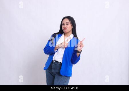 Der Charme einer schönen jungen indonesischen Bürofrau, die einen blauen formalen Anzug trägt und die Stirn runzelnd mit beiden Händen nach oben links zeigt. Für Corpo Stockfoto