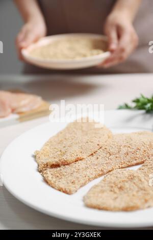 Frau, die Schnitzel am hellen Holztisch macht, konzentriert euch auf Fleischscheiben mit Brotkrümeln Stockfoto